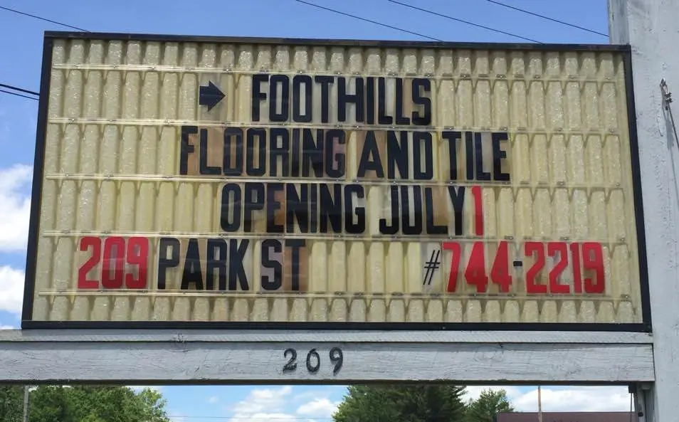 image shows a sign for Foothills Flooring and Tile, announcing its opening on July 1st, at 209 Park St, with the phone number 744-2219